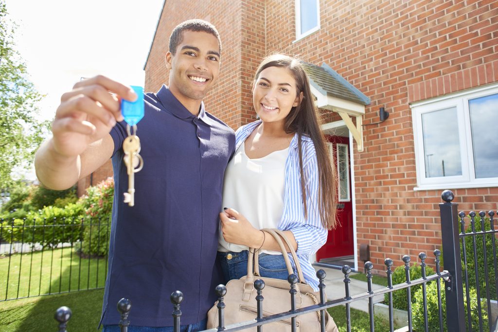 a couple hold their keys aloft in front of their new home