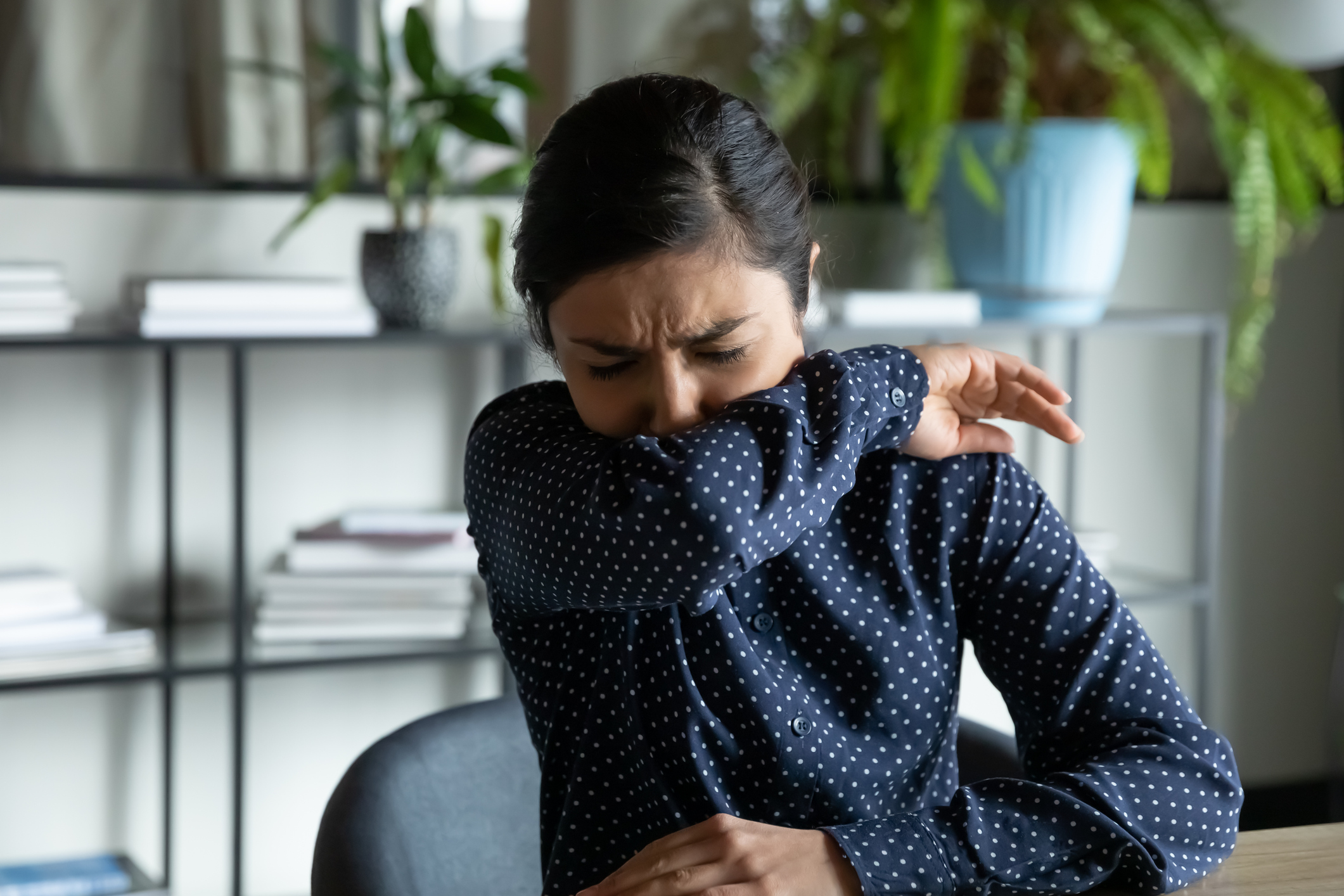 A woman coughs into her elbow.