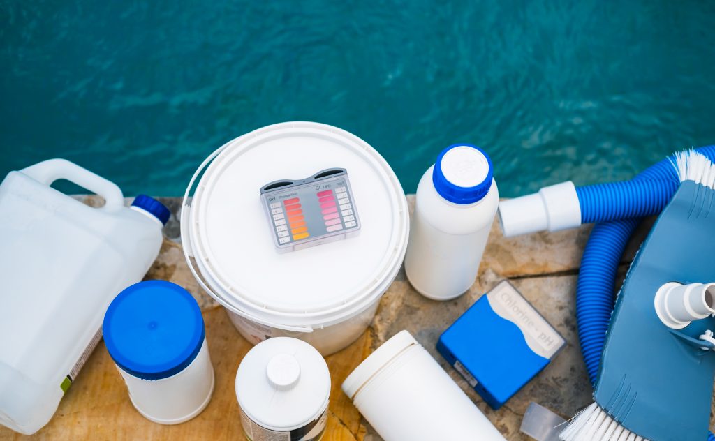 High angle view of equipment for testing the quality of pool water, vacuum cleaner and chemical cleaning products at the edge of swimming pool.
