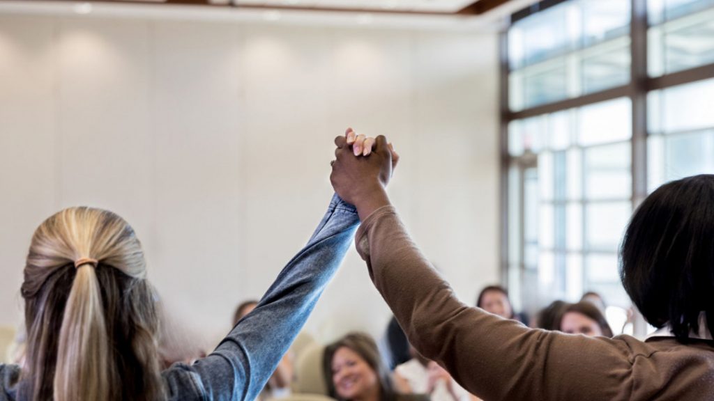 Women holding hands empowering each other in front of an audience.