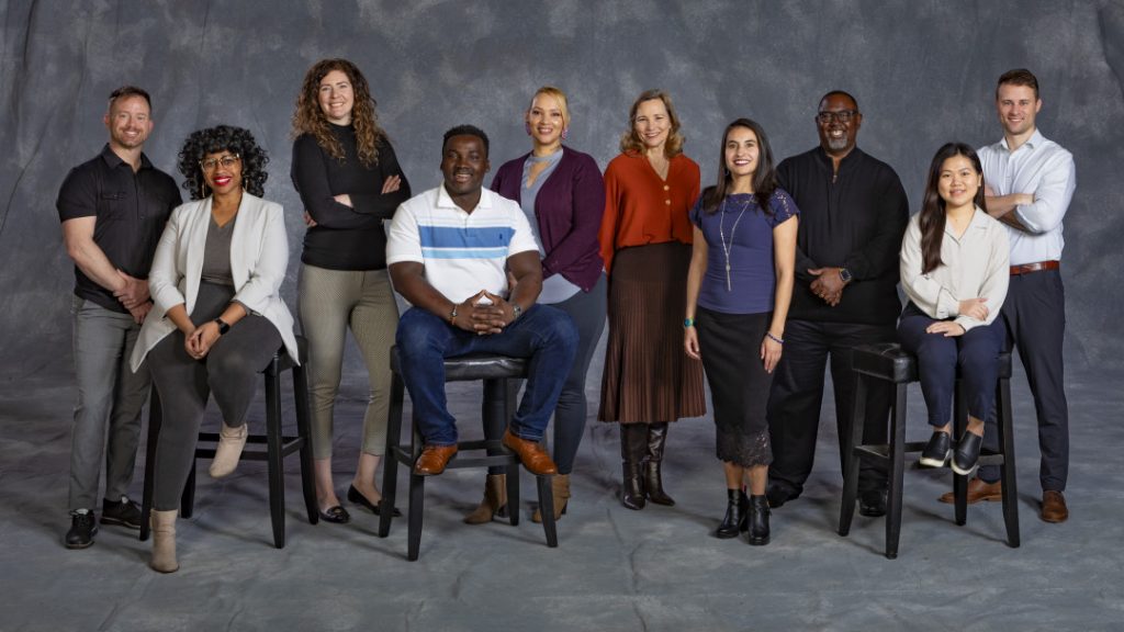 Various THD staff members stand and sit in front of gray background