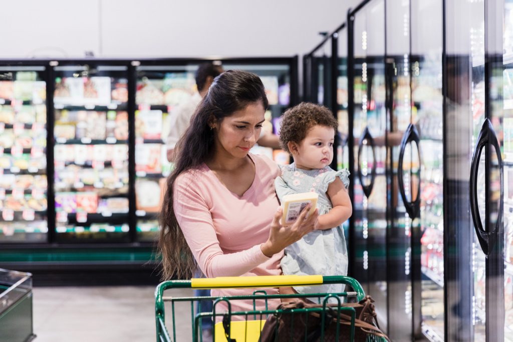 The young mother holds onto her child as she grocery shops for a new product she has been searching for.